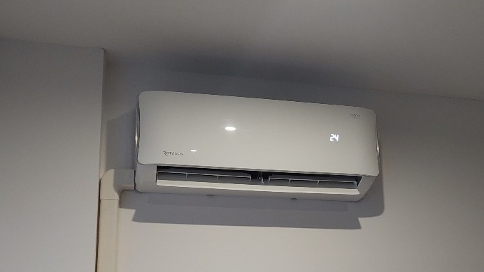Biała jednostka klimatyzacji Rotenso zamontowana na ścianie w pomieszczeniu, widoczny wyświetlacz temperatury wskazujący 24 stopnie Celsjusza, z widoczną maskownicą instalacji elektrycznej.