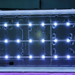 Wnętrze obudowy telewizora z zamontowanymi, świecącymi listwami LED podświetlającymi matrycę. Widoczne przewody i elementy mocujące listwy.