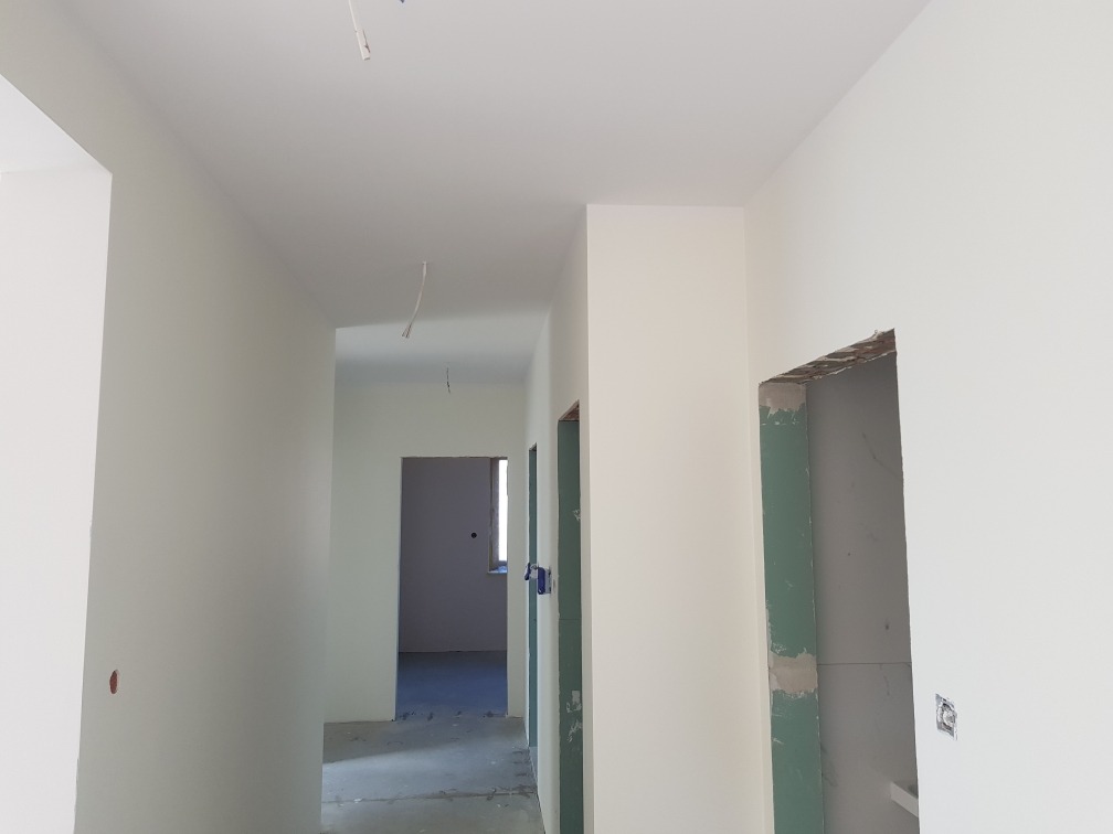 Korytarz w trakcie wykańczania: świeżo pomalowane ściany w jasnym odcieniu, surowa ościeżnica drzwiowa, widok na kolejne pomieszczenia w głębi.