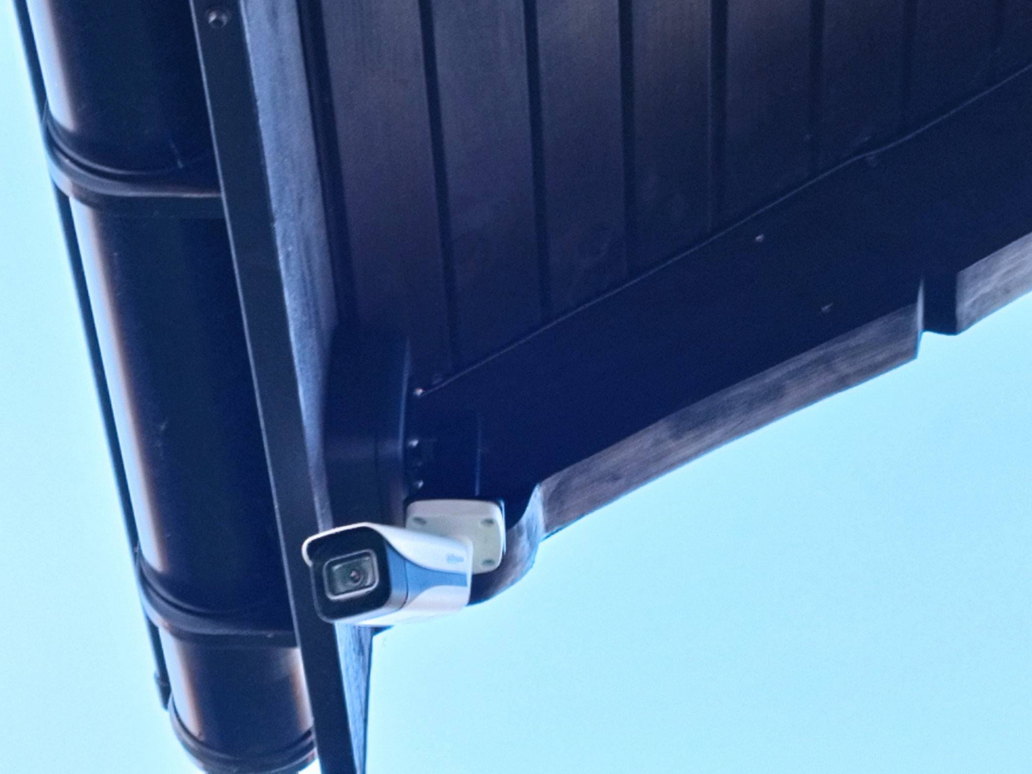 Kamera przemysłowa zamontowana pod okapem dachu, widok z dołu na błękitne niebo.