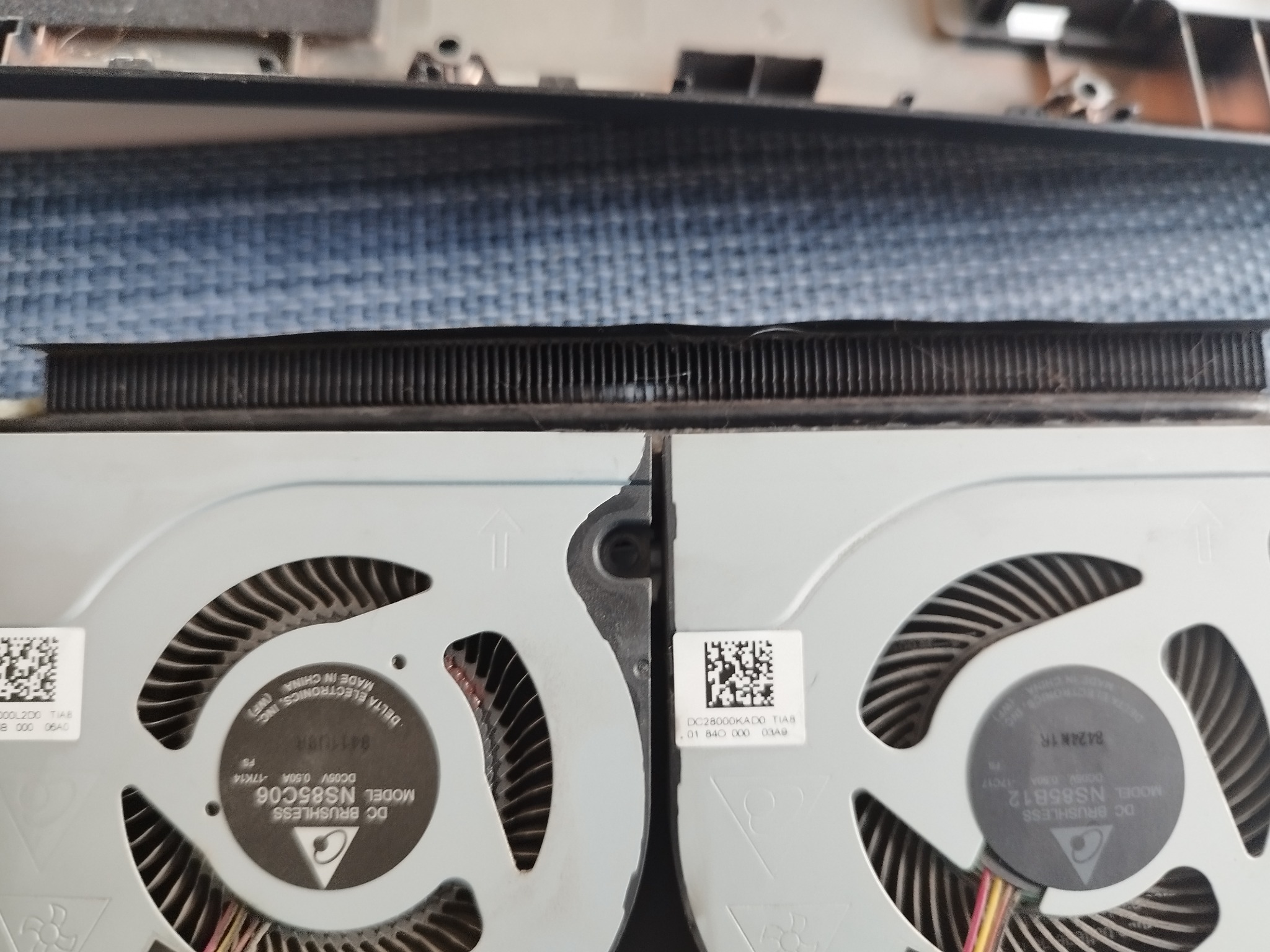Wnętrze laptopa z widocznymi dwoma wentylatorami chłodzącymi procesor i radiatorem, widoczne naklejki z kodami QR i oznaczeniami modeli wentylatorów.