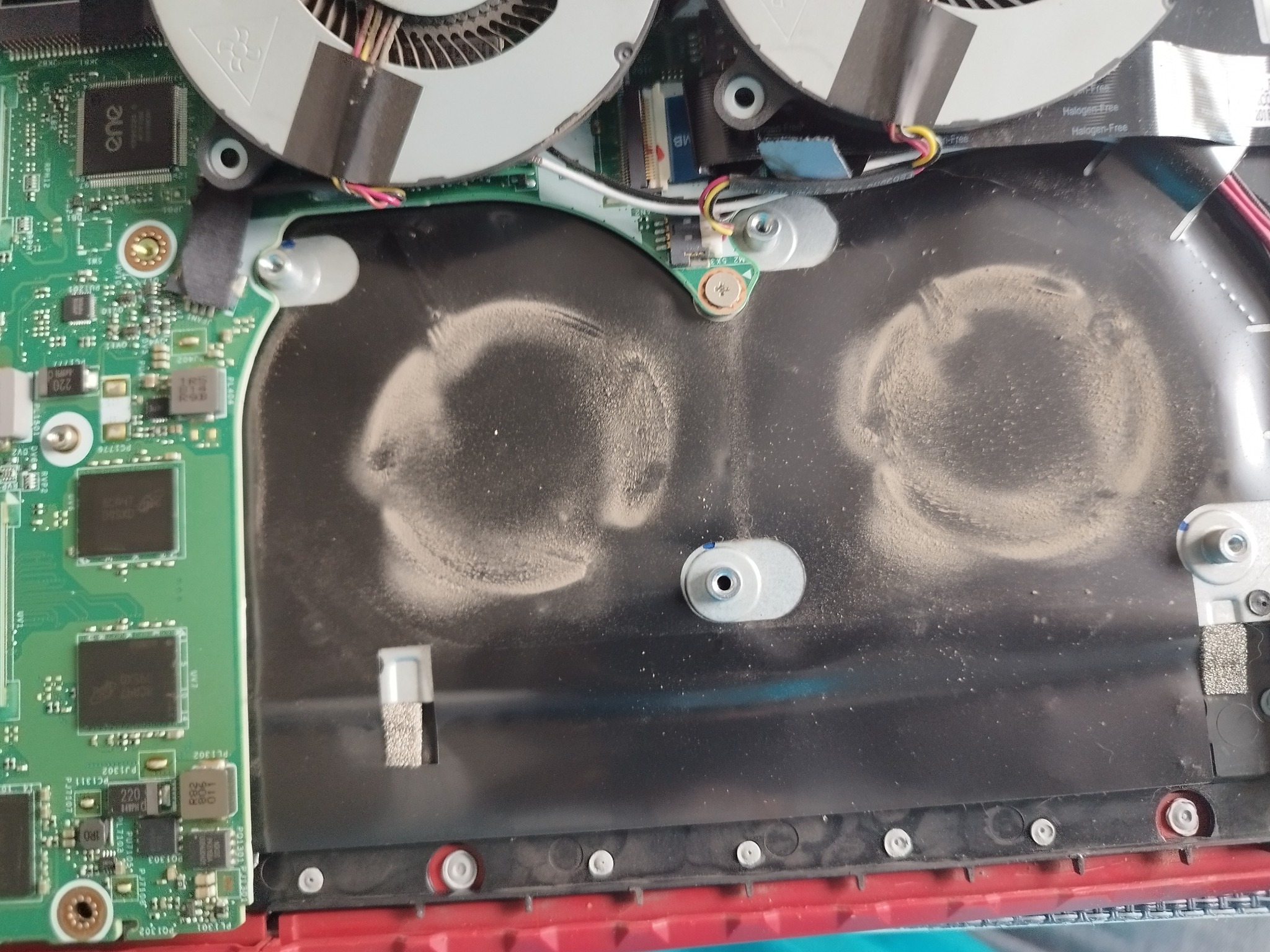 Wnętrze laptopa z widocznymi wentylatorami i zakurzoną płytą główną, wymagające czyszczenia w celu poprawy chłodzenia.