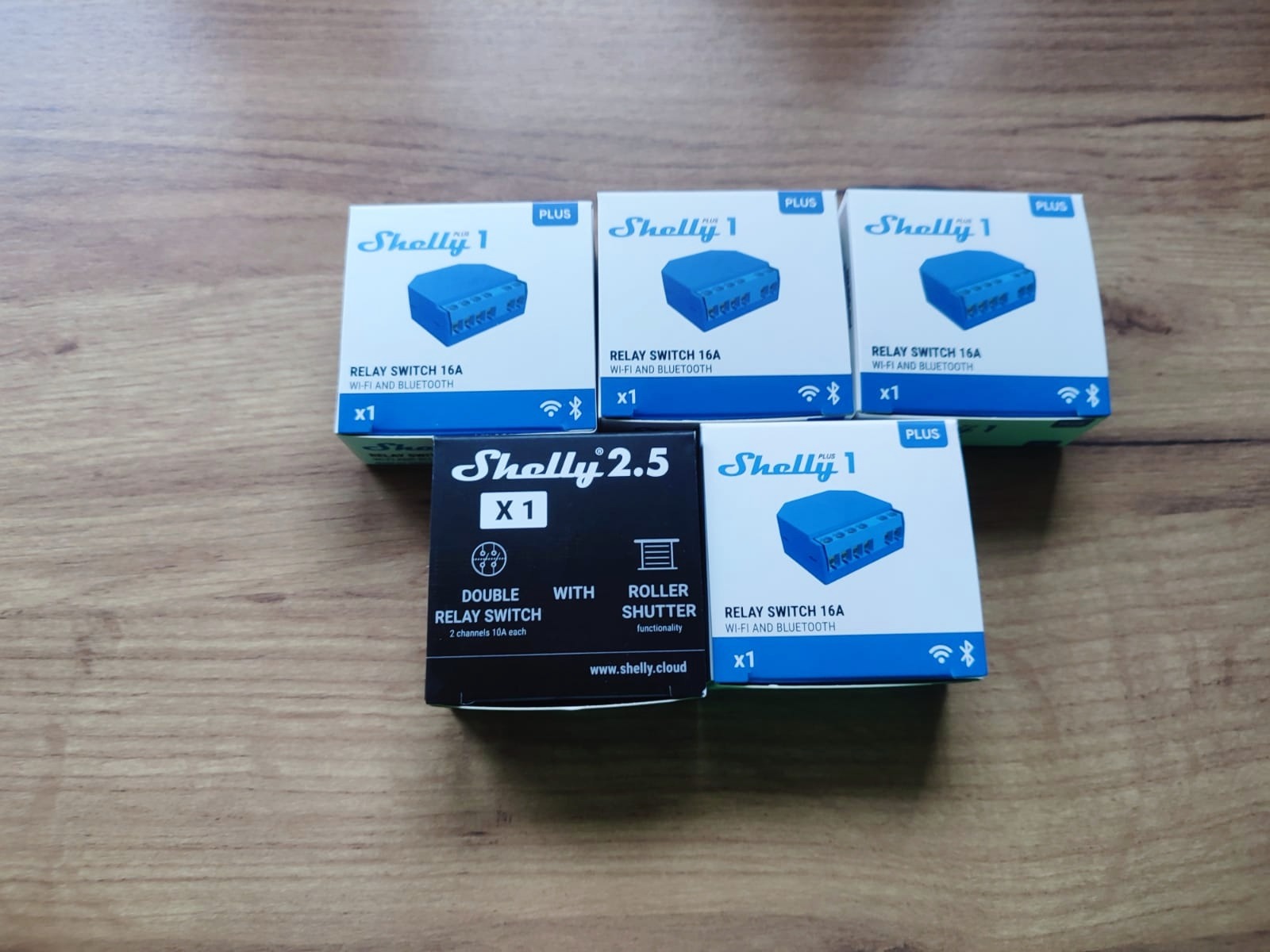 Pudełka z modułami Shelly 1 Plus i Shelly 2.5 do inteligentnego domu, leżące na drewnianej powierzchni.