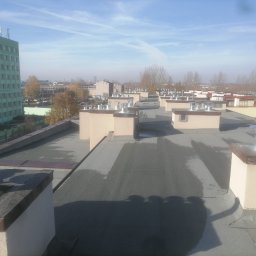 MUR-BETON MICHAŁ KLIMEK - Widok z góry na płaski dach budynku z kominami wentylacyjnymi, w tle budynek biurowy Elbud Katowice i zabudowa miejska w lekkiej mgle.