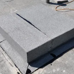 Szczegółowe ujęcie obróbki blacharskiej komina na płaskim dachu pokrytym papą termozgrzewalną, widoczny butla z gazem i palnik.