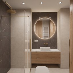 Sroka Design Projektowanie Wnętrz Klaudia Sroka - Nowoczesna łazienka z okrągłym lustrem podświetlanym LED, brązowymi płytkami imitującymi marmur i drewnianą szafką. Kabina prysznicowa ze złotymi elementami.