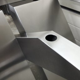 HEFTdesign Paweł Wojewodzic - Metalowa konstrukcja z otworami, prawdopodobnie fragment balustrady lub poręczy, wykonana z polerowanej stali. Widoczne ostre krawędzie i precyzyjne wykonanie.