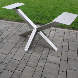 HEFTdesign Paweł Wojewodzic - Metalowy stelaż stołu z kwadratowymi podstawami, ustawiony na szarej kostce brukowej, z zielonym trawnikiem w tle. Widok z góry, ukazujący krzyżową konstrukcję.