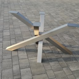 HEFTdesign Paweł Wojewodzic - Nowoczesna, geometryczna podstawa stołu z metalu, z trzema ramionami krzyżującymi się pod kątem. Wykończenie w odcieniach szarości i srebra, na tle szarej kostki brukowej.