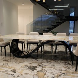HEFTdesign Paweł Wojewodzic - Stylowa jadalnia z marmurowym stołem na czarnej, designerskiej podstawie. W tle schody z szklaną balustradą i nowoczesne oświetlenie.