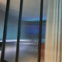 Przesuwne drzwi szafy wnękowej z ryflowanego szkła w ciemnej metalowej ramie.