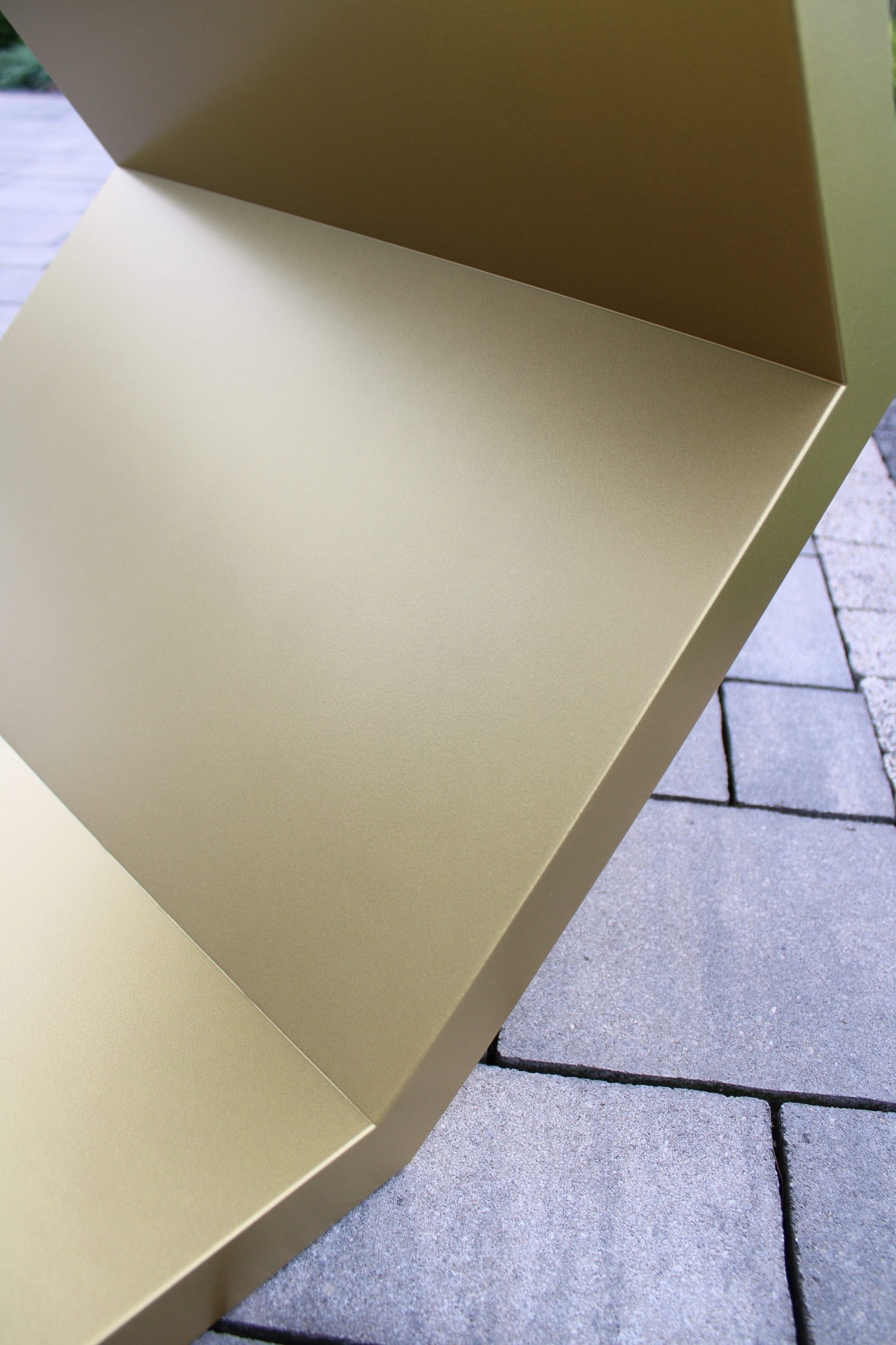 Fragment złotej, geometrycznej konstrukcji metalowej na tle szarej kostki brukowej, prezentujący precyzję wykonania i nowoczesny design.