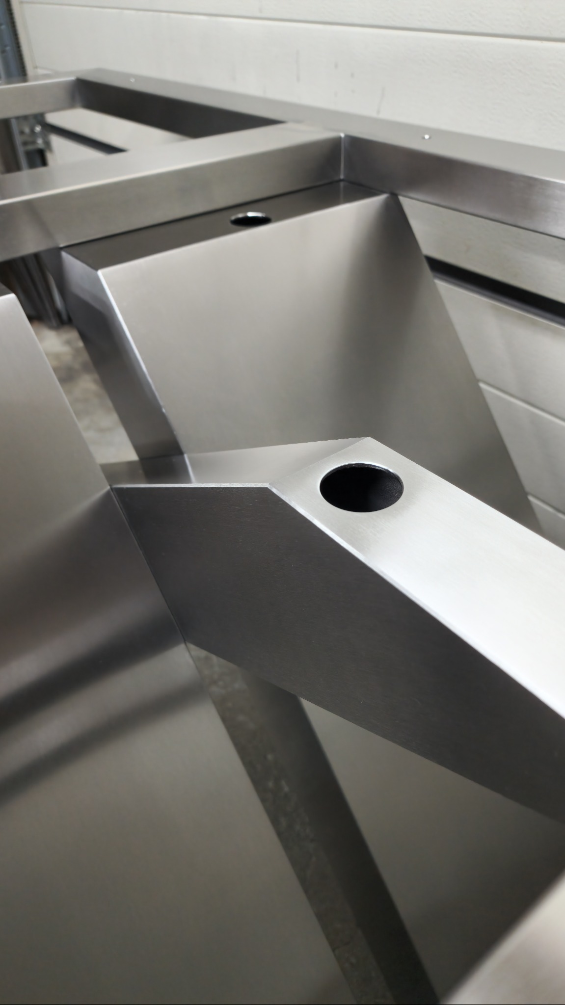 Metalowa konstrukcja z otworami, prawdopodobnie fragment balustrady lub poręczy, wykonana z polerowanej stali. Widoczne ostre krawędzie i precyzyjne wykonanie.