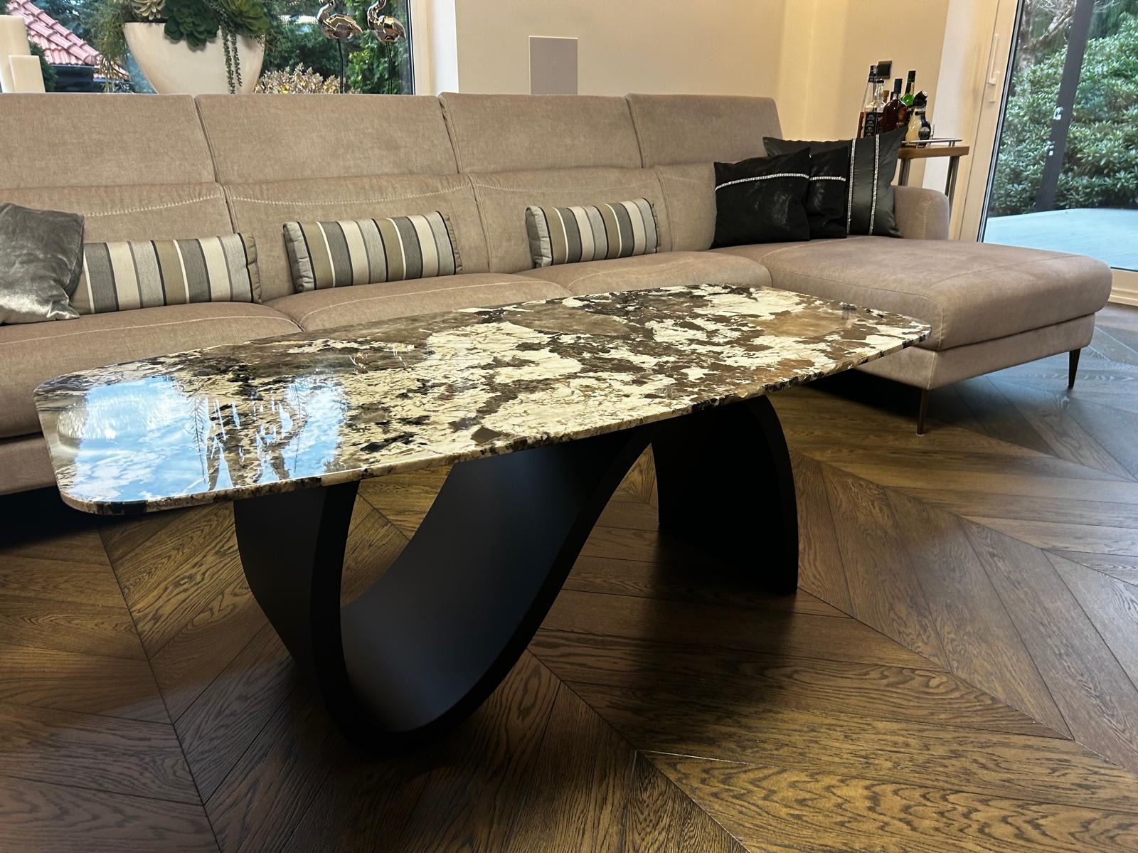 Stylowy stolik kawowy z blatem imitującym marmur i oryginalną, czarną podstawą na tle salonu z parkietem w jodełkę i beżową sofą.