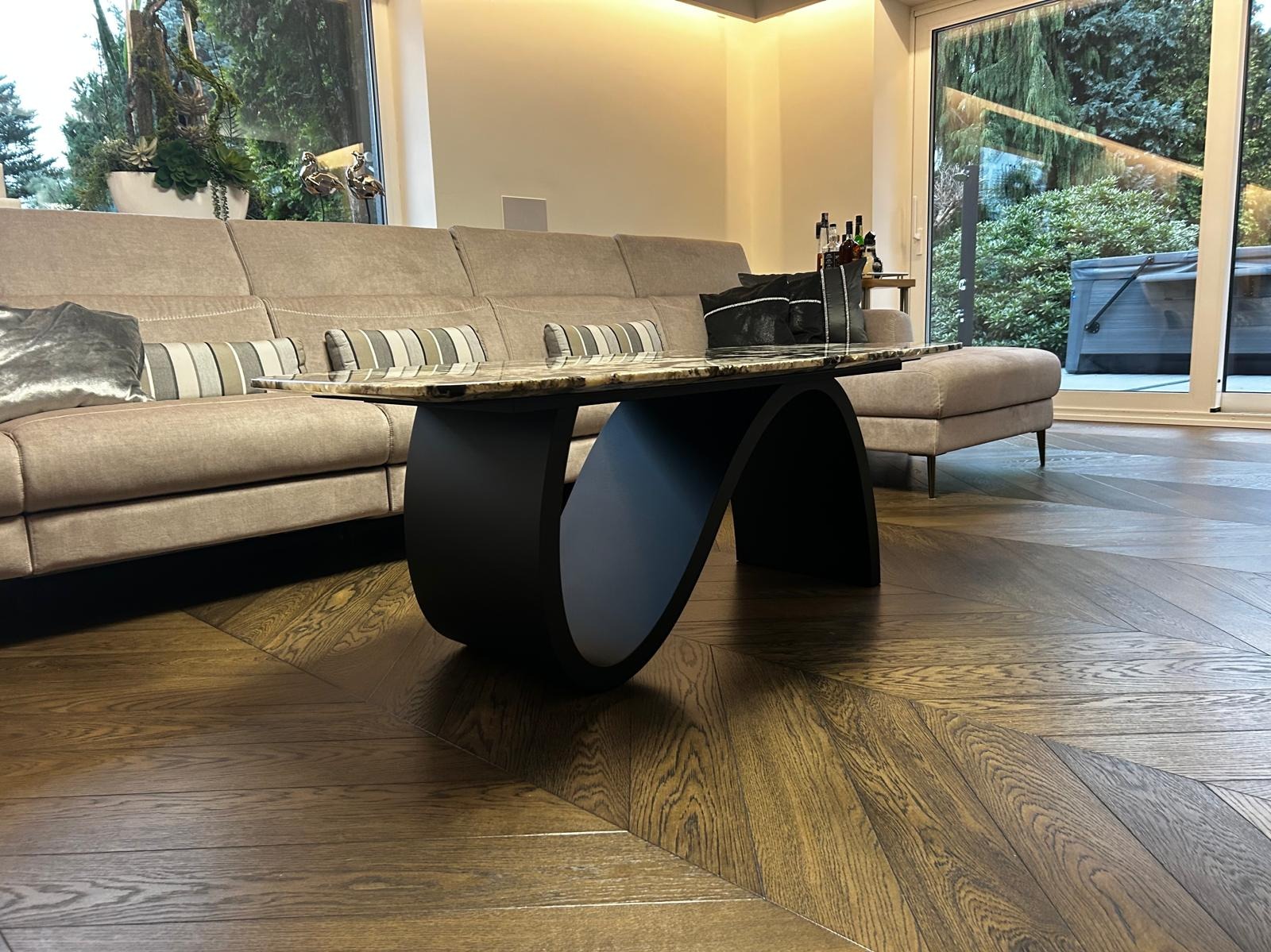 Stylowy stolik kawowy z marmurowym blatem i czarną, zakrzywioną podstawą w nowoczesnym salonie z parkietem w jodełkę i widokiem na zewnątrz.