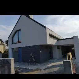 Nowoczesny dom jednorodzinny z jasnoszarą elewacją, ciemnoszarym panelem elewacyjnym, schodami i aluminiową drabiną opartą o ścianę, w trakcie prac wykończeniowych.