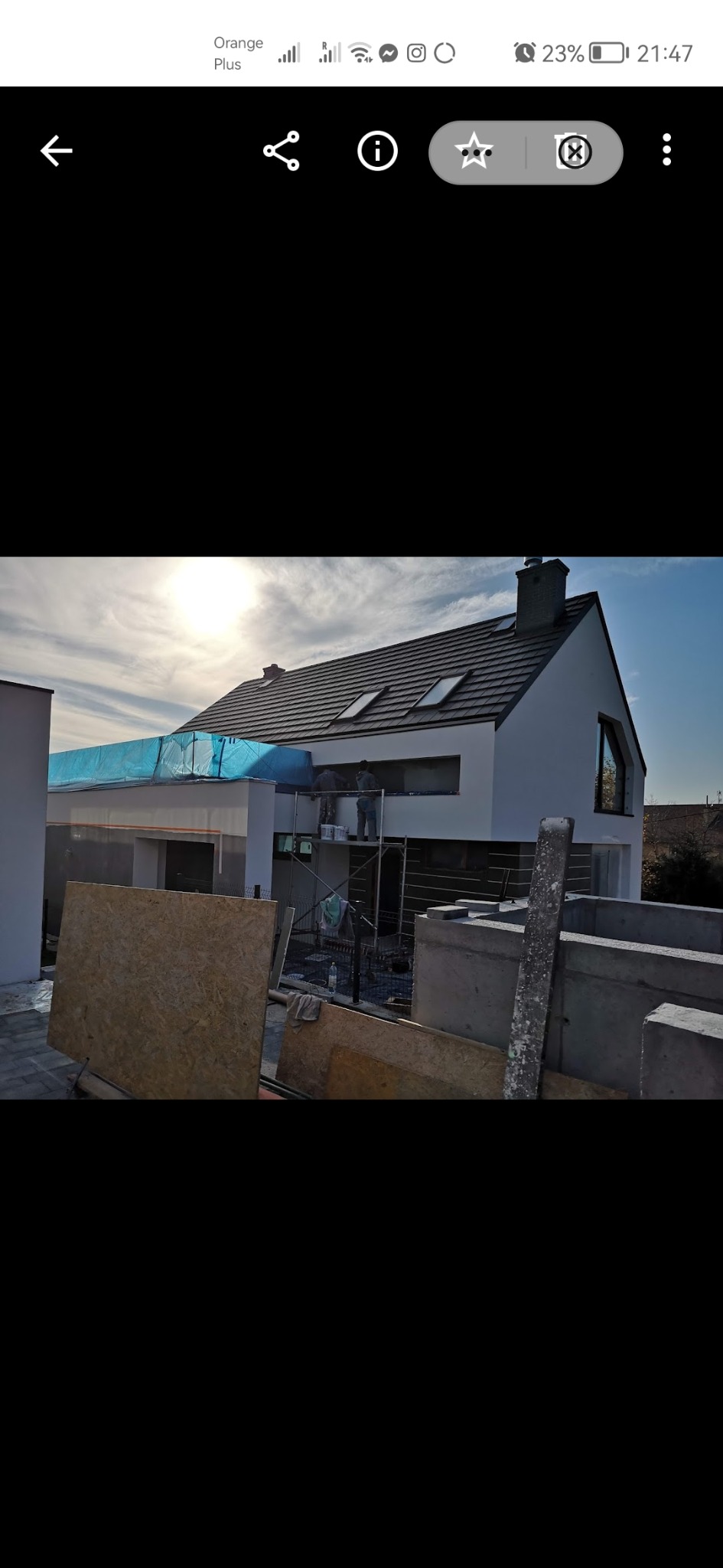 Nowoczesny dom jednorodzinny w trakcie wykończenia elewacji, widoczne rusztowania i materiały budowlane, fragment zabezpieczonego dachu folią ochronną.