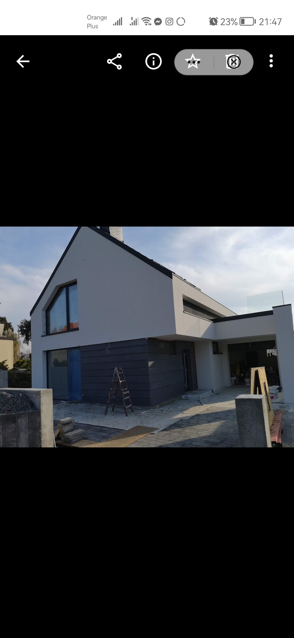 Nowoczesny dom jednorodzinny z jasnoszarą elewacją, ciemnoszarym panelem elewacyjnym, schodami i aluminiową drabiną opartą o ścianę, w trakcie prac wykończeniowych.