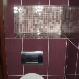 Wykończona toaleta w łazience z bordowymi płytkami, wbudowana półka z mozaiką i chromowany przycisk spłuczki.