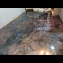 AUTO CZĘŚCI FIREK - MARCIN FIREK - Błyszcząca, wielobarwna posadzka żywiczna w pomieszczeniu po remoncie. Widoczne ślady po pracach wykończeniowych na ścianach i podłodze. Nietypowe wykończenie podłogi.