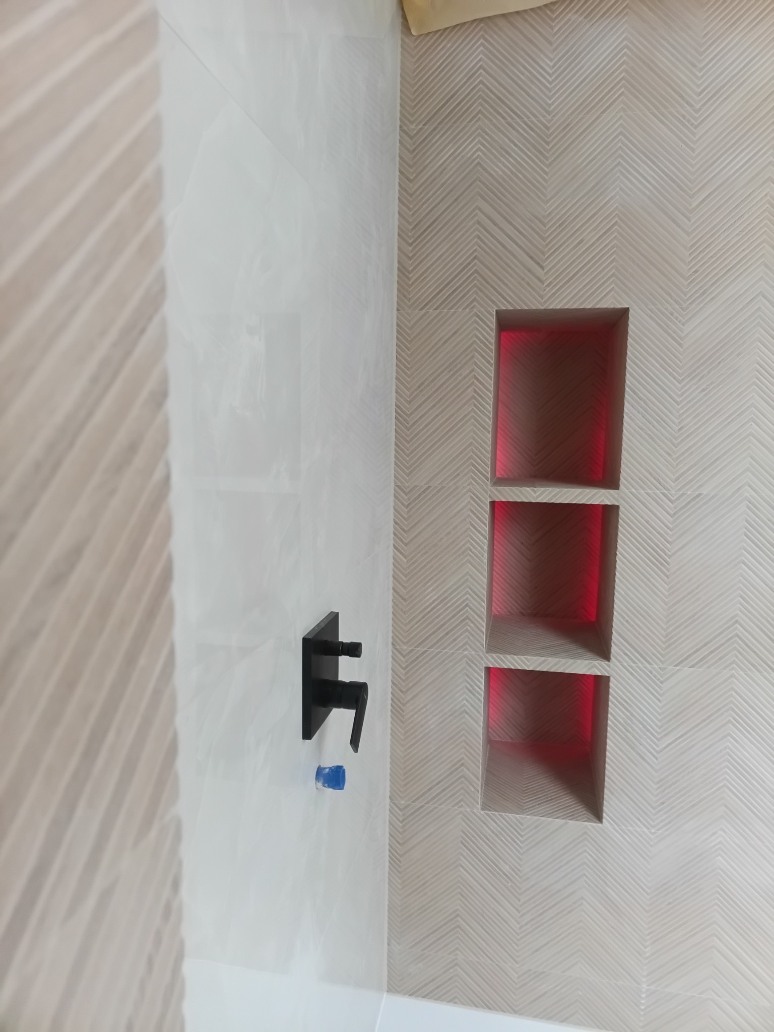 Nowoczesna łazienka z geometrycznym wzorem na ścianie, wnękami z czerwonym podświetleniem i czarną armaturą. Minimalistyczny design, jasne kolory, ukończony projekt.