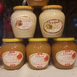 Piramida z słoików różnych rodzajów miodu, w tle choinka z ozdobami, etykiety widoczne.