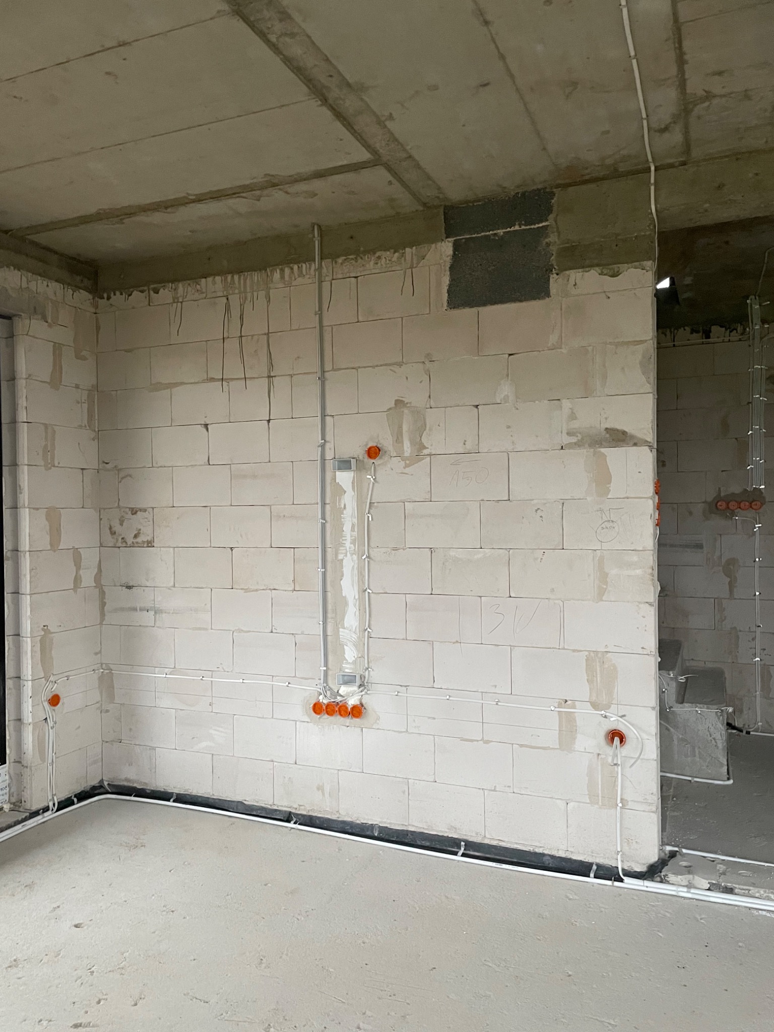 Wewnętrzne okablowanie elektryczne w surowym stanie, widoczne puszki instalacyjne i kable prowadzone po ścianach z bloczków betonowych, przygotowane do dalszych prac wykończeniowych.