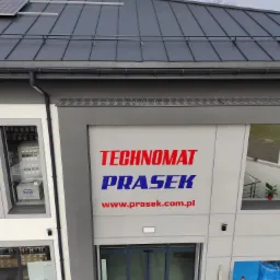 Elewacja budynku firmy Technomat Prasek z widocznym logo i adresem strony internetowej, panele słoneczne na dachu, okna wystawowe z ekspozycją produktów.