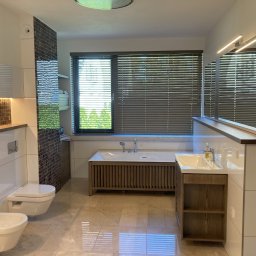 Pracownia Stolarska Podpirka - Nowoczesna łazienka z beżowymi płytkami podłogowymi, wiszącą toaletą i bidetem, wanną obudowaną drewnianymi listwami oraz szafką umywalkową z drewnianymi akcentami, oświetlona listwami LED...