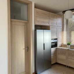 Pracownia Stolarska Podpirka - Jasna kuchnia z drewnianymi szafkami, zabudowaną lodówką side-by-side i drzwiami wewnętrznymi z przeszkleniem u góry, podłoga z jasnego marmuru.