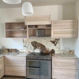 Pracownia Stolarska Podpirka - Jasna kuchnia z drewnianymi frontami, marmurowym blatem i backsplashiem z unikalnym wzorem przypominającym mapę, oświetlona przez dwie wiszące lampy w kształcie kropli.