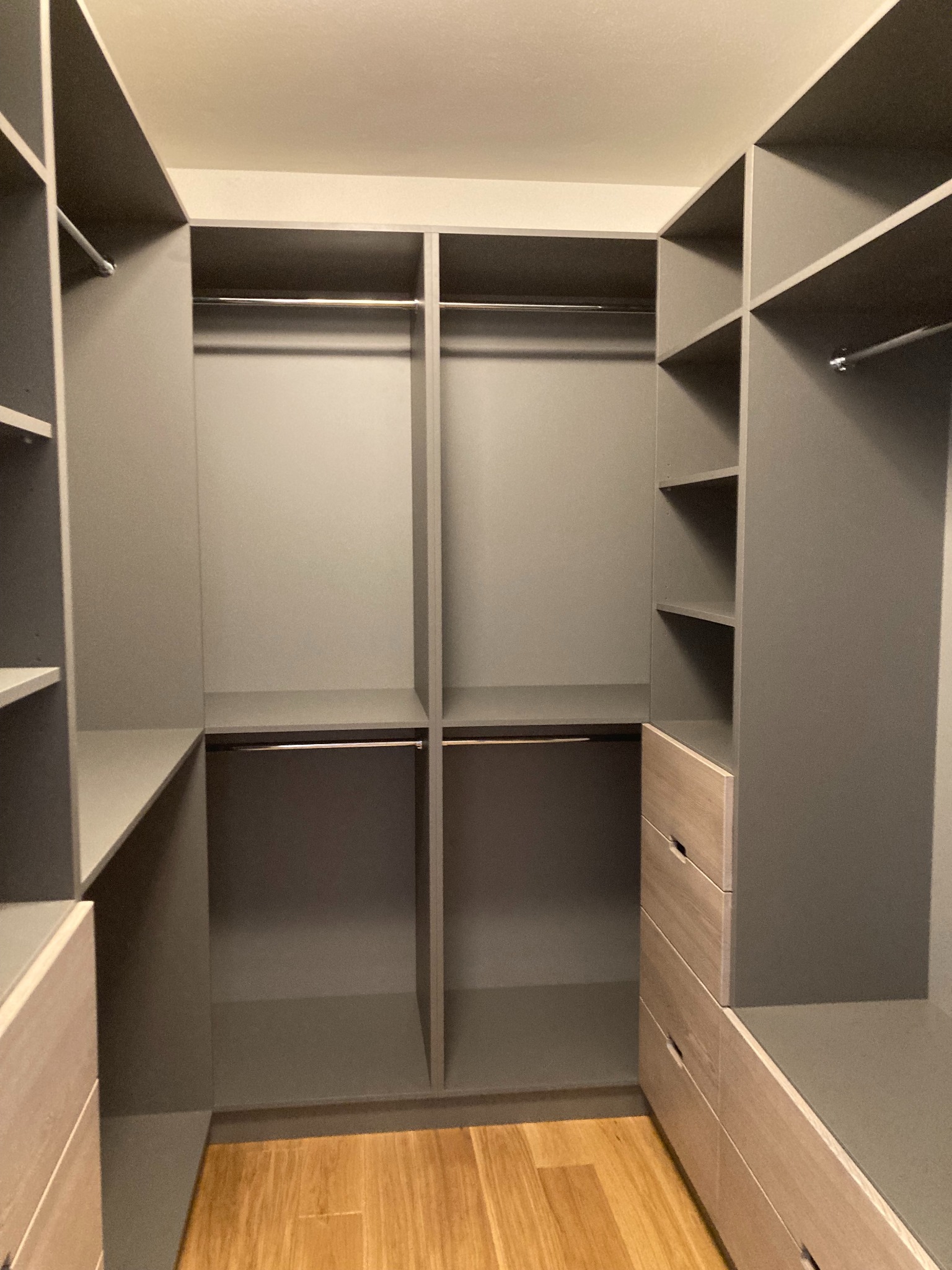 Pusta garderoba w odcieniach szarości z drewnianymi szufladami i podłogą, widok na półki i drążki na ubrania.