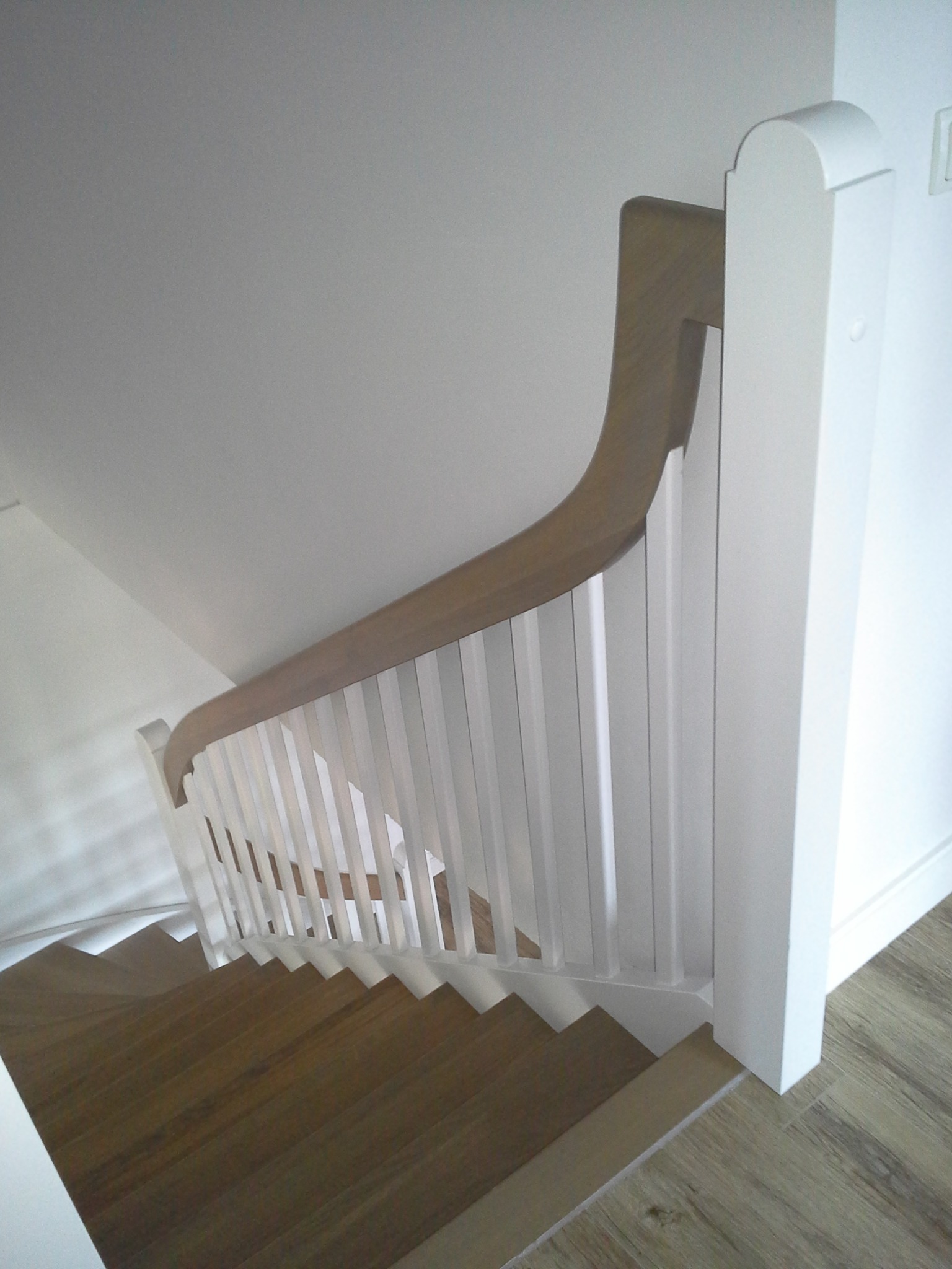 Drewniane schody z białymi balustradami i drewnianą poręczą, widok z góry, oświetlenie naturalne, minimalistyczny styl.