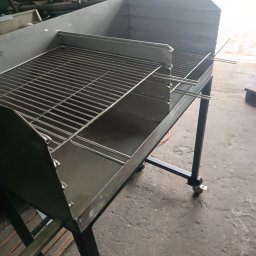 Hartmet - Metalowy grill na kółkach z rusztem, wykonany ze stali, w warsztacie z widocznymi śladami użytkowania na podłodze.