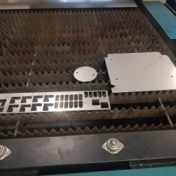 Hartmet - Metalowe elementy o różnych kształtach (okrąg, prostokąt z wycięciami, kwadrat z otworami) leżą na stole roboczym maszyny do obróbki metali.