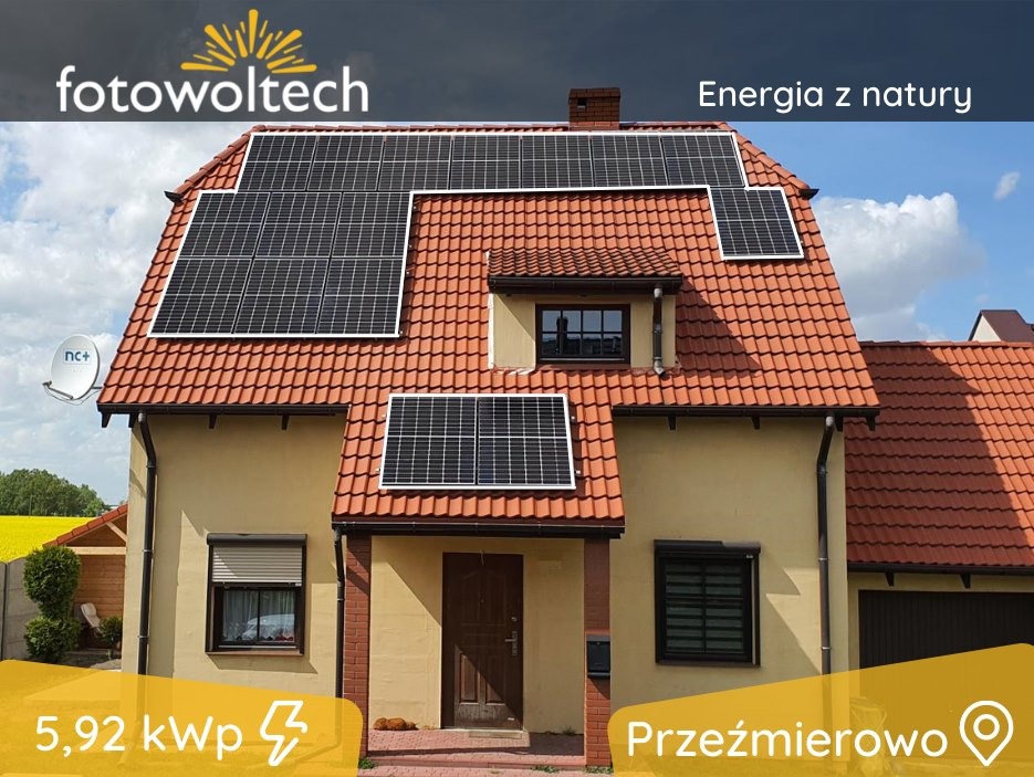 Dom jednorodzinny z panelami słonecznymi na dachu pokrytym czerwoną dachówką. Widoczna antena satelitarna, żółte pole w tle i oznaczenie 5,92 kWp.