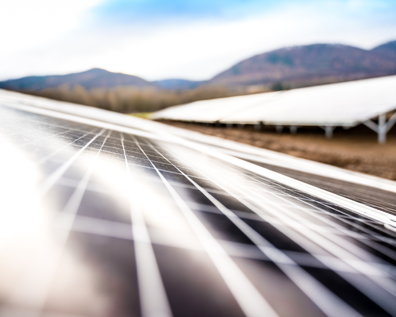 Detaliczny widok paneli fotowoltaicznych na tle pagórkowatego krajobrazu pod błękitnym niebem.