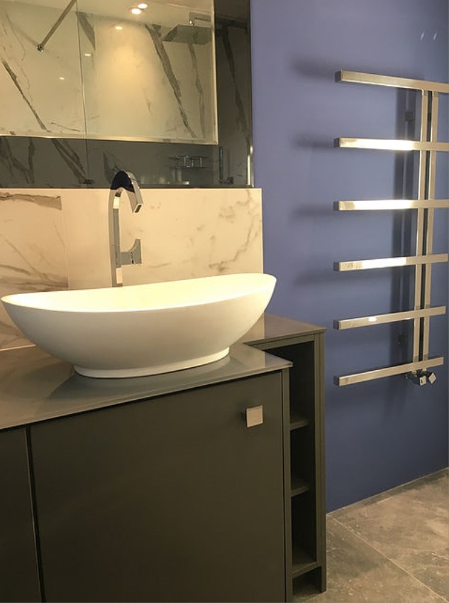 Nowoczesna łazienka z owalną umywalką nablatową, szafką w kolorze grafitowym i grzejnikiem drabinkowym na niebieskiej ścianie, wykończona marmurem.