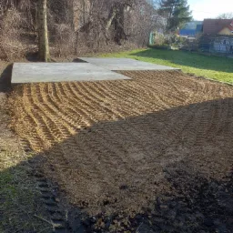 Przygotowany teren pod wylewkę fundamentów w Tarnowie, widoczne ślady opon ciężkiego sprzętu i wyrównana powierzchnia z piasku.