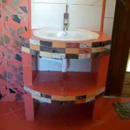 Łazienka z umywalką na postumencie z pomarańczowych płytek, zdobionym mozaiką, na tle ściany z płytek w liście