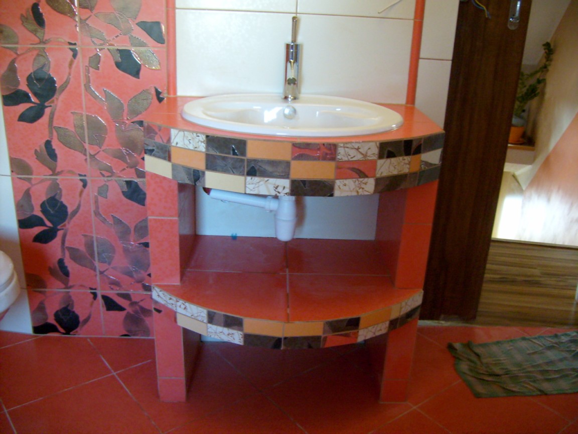 Łazienka z umywalką na postumencie z pomarańczowych płytek, zdobionym mozaiką, na tle ściany z płytek w liście