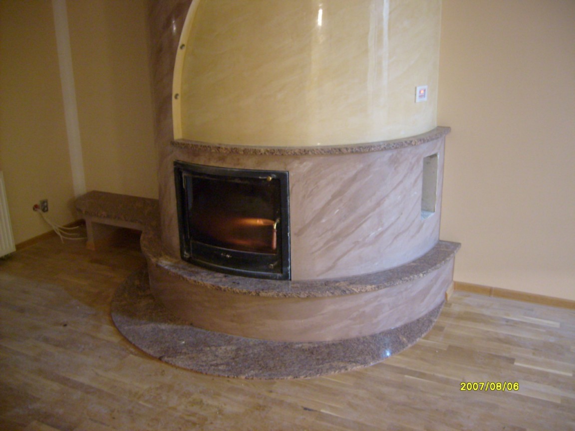 Okrągły kominek z marmurową obudową, z palącym się wewnątrz ogniem, w pokoju z drewnianą podłogą i kremowymi ścianami.