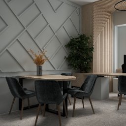 Emilia Kozłowska Projekty z Pasją - Stylowa aranżacja biura: stół z krzesłami na tle ściany z geometrycznym wzorem i drewnianej boazerii. Wazon z suchymi kwiatami i zielona roślina dodają charakteru.