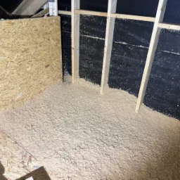 Poddasze z widoczną warstwą izolacji celulozowej, czarna membrana i drewniane elementy konstrukcyjne. Gotowa realizacja ocieplenia.