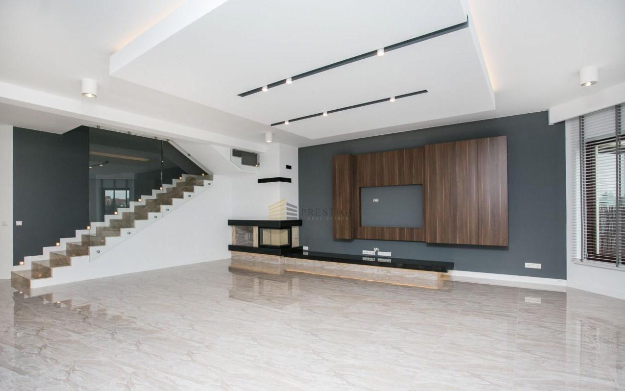 Przestronne wnętrze w Warszawie po remoncie: marmurowe płytki podłogowe, schody z podświetleniem LED, ściana akcentowa w odcieniach szarości z drewnianą zabudową TV oraz nowoczesny kominek.