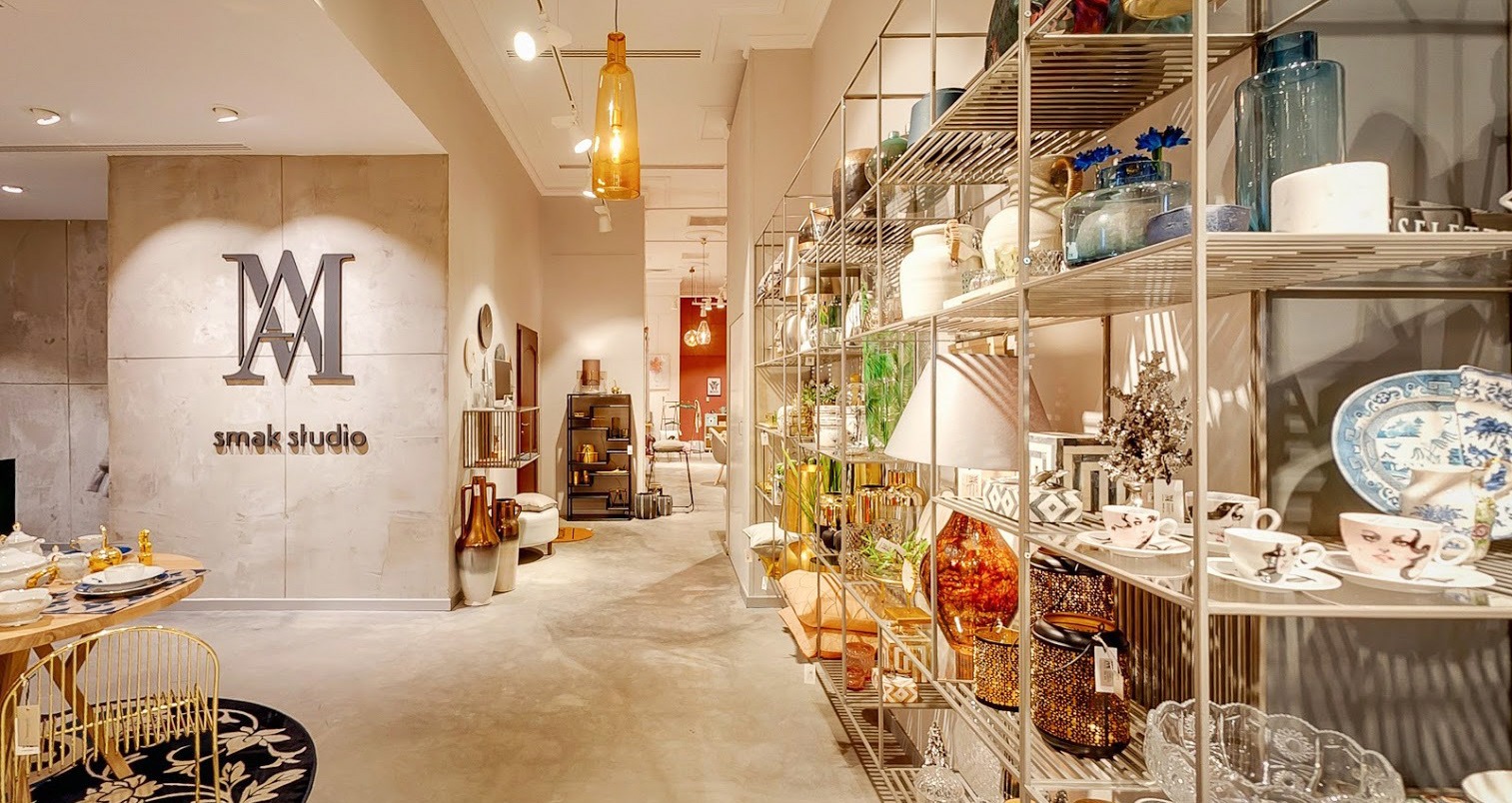 Wnętrze sklepu Smak Studio z metalowymi regałami pełnymi dekoracji, naczyń i wazonów, w tle widoczny korytarz z oświetleniem punktowym.