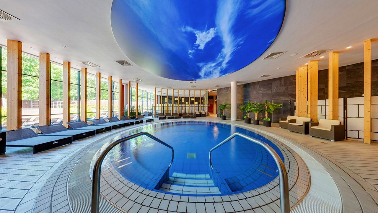 Wnętrze luksusowego basenu w Łodzi z leżakami, sofami i dekoracyjnym sufitem z motywem nieba.
