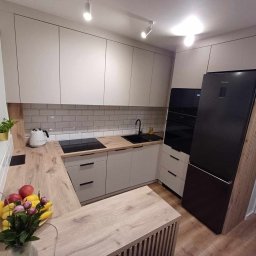 Stylove Kuchnie - Jasna kuchnia z drewnianym blatem, czarnym zlewem i sprzętem AGD, oświetlona punktowymi lampami sufitowymi, z owocami i kwiatami na blacie.