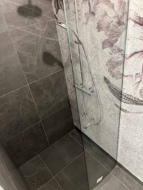 Nowoczesna kabina prysznicowa z szarymi płytkami imitującymi marmur i ścianą z dekoracyjną tapetą w kwiatowe wzory, widok z góry.