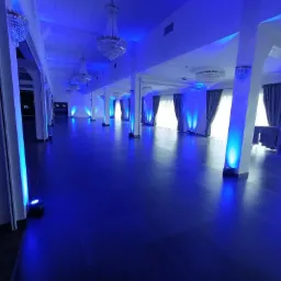 Pusta sala balowa z kryształowymi żyrandolami i kolumnami oświetlonymi niebieskim światłem LED.